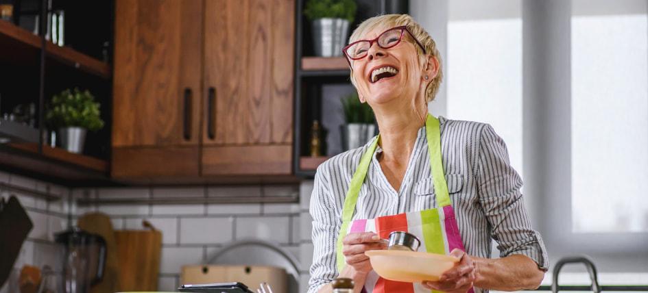 A Guide to Nutrition in Recovery - an image of an older woman cooking in the kitchen, looking content and laughing