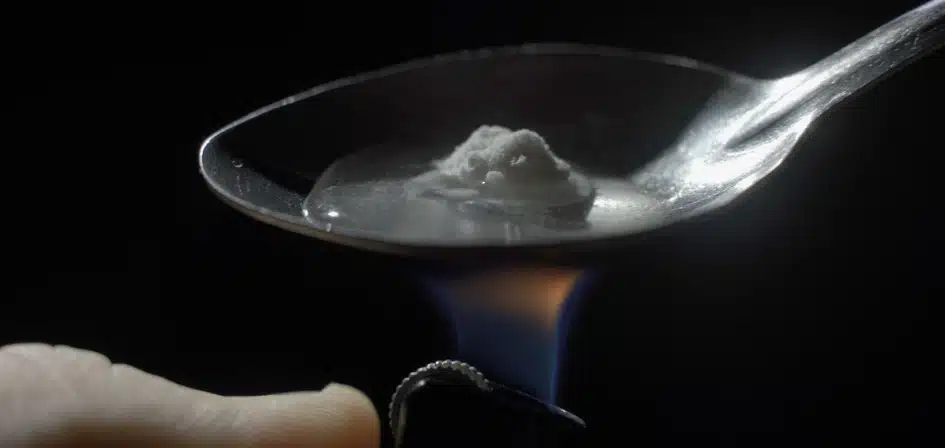 How Long Does Heroin Stay in Your System? An image of a man's hand sets fire the lighter over spoon of boiling drug, diluted heroin.