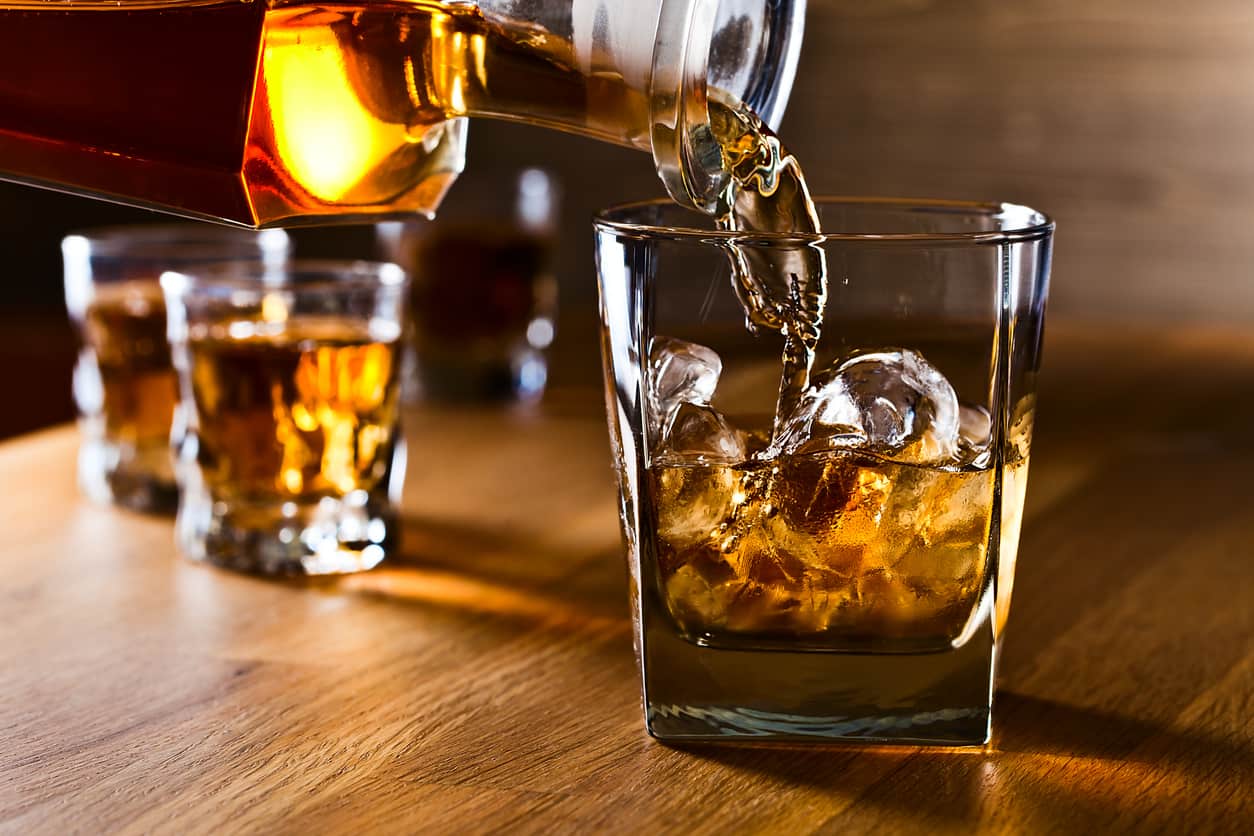 Whiskey being poured into small glass with ice