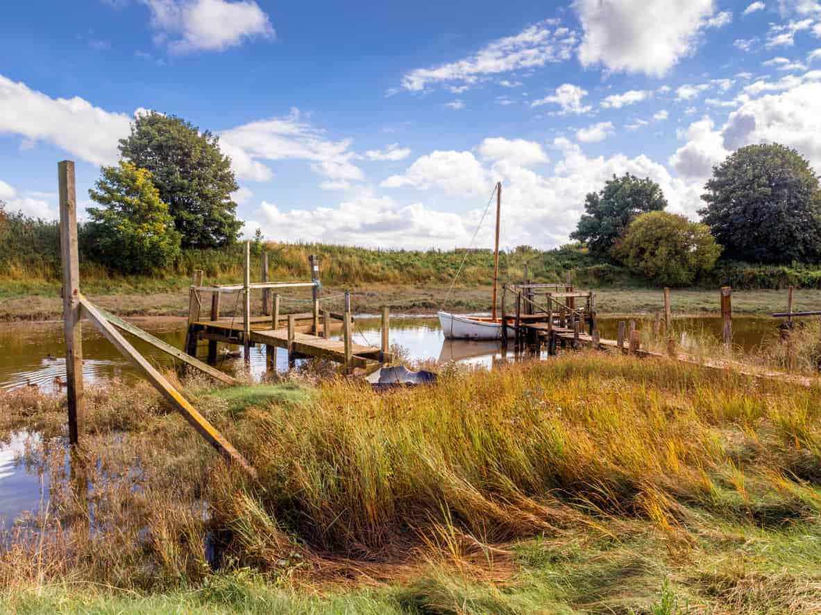 Old wooden small boat dock on shallow water encompassed by fields and trees