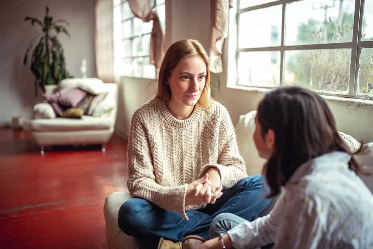 Two women sat on sofa, one confiding in the other