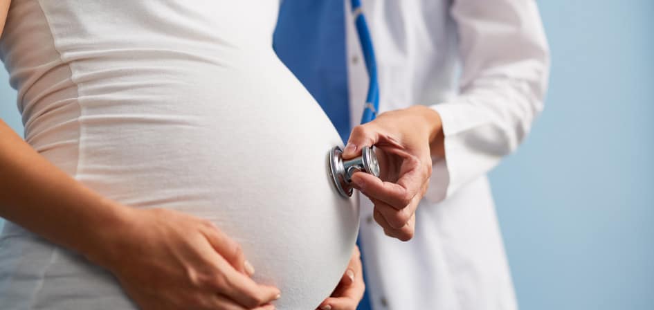 Does Your Body Reject Alcohol When Pregnant - an image of a woman who is pregnant, with a close up of the bump and a doctor listening to the heartbeat using a stethoscope