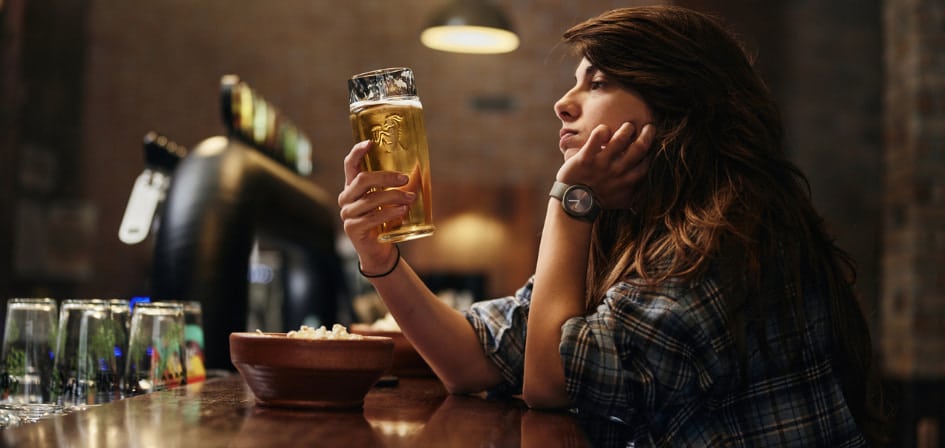 Is Getting Drunk and Saying Hurtful Things Normal - an image of a woman drinking beer alone at the bar, staring at the drink in her hand whilst looking serious.