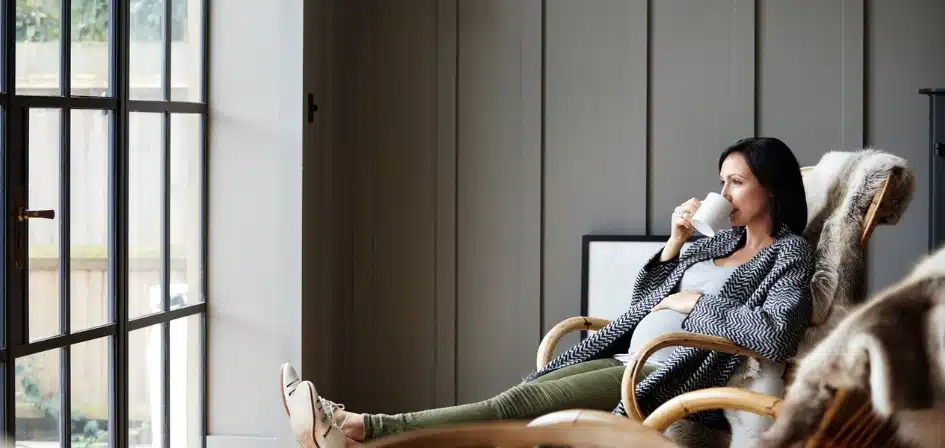 The Risks of Drinking in Early Pregnancy Without Knowing. An image of a pregnant woman drinking tea while relaxing on a rocking chair at home