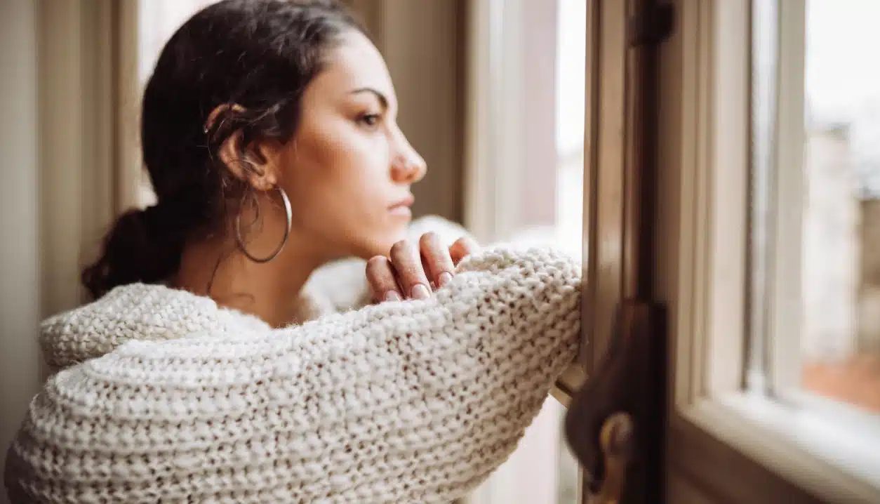 Life After Addiction How to Cope With Survivor’s Guilt. An image of a woman looking out the window looking serious.