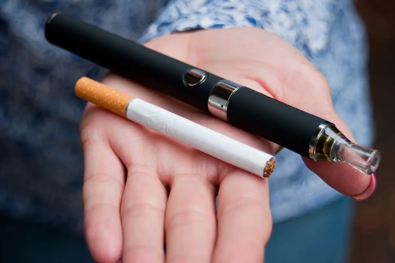 A person holding a cigarette and a vape