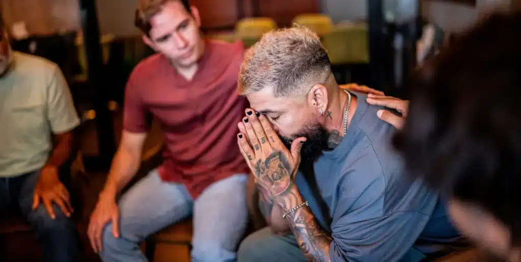 Is Addiction Considered a Chronic Illness? Image of a man being comforted in a group therapy