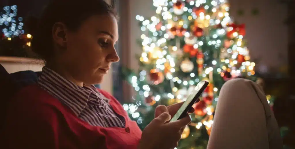 A woman experiencing loneliness at Christmas, scrolling on her phone