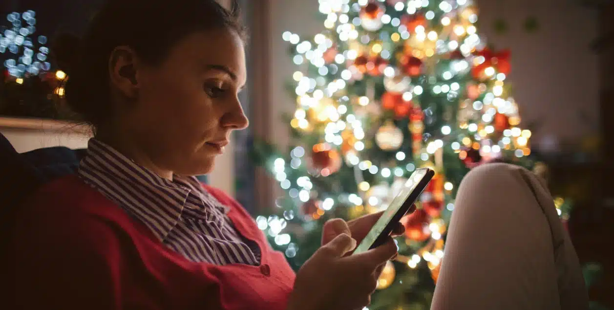 A woman experiencing loneliness at Christmas, scrolling on her phone