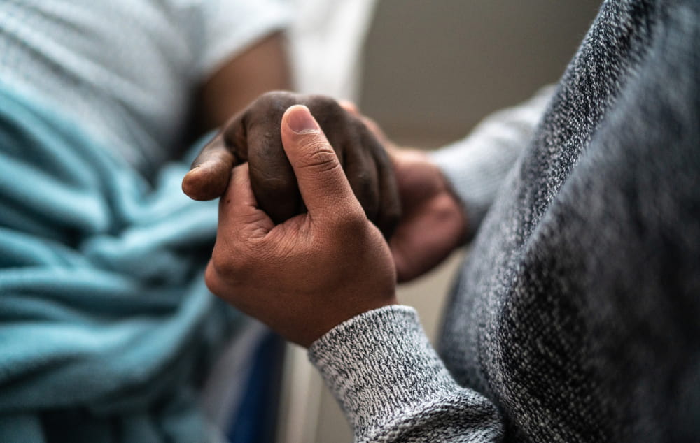 close-up of person's hand holding the hand of someone in a hospital bed
